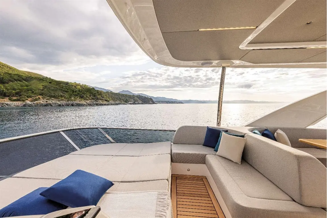 Luxurious yacht seating area with plush cushions overlooks tranquil waters and green hills under a cloudy sky.